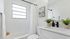 Bright and elegant bathroom showcasing a pristine white design, featuring a modern vanity with sleek fixtures, stylish picture, and decorative plants for a fresh ambiance.