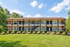 Charming two-story apartment building with spacious balconies, surrounded by lush greenery and vibrant landscaping under a bright blue sky.