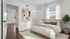 Bright bedroom featuring a cozy bed with neutral throw pillows, elegant abstract art on the wall, and a lush potted plant by the window, offering a serene and inviting atmosphere.