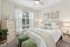 Bright and cozy bedroom with elegant decor, featuring a plush bed, stylish wooden dresser, and large window with sheer curtains.