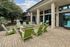 Inviting outdoor patio area with stylish green chairs around a cozy fire pit, surrounded by lush greenery and modern stone architecture.