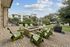 Charming outdoor patio with green chairs surrounding a stone fire pit, set in a lush landscaped garden, perfect for relaxation and social gatherings.