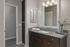 Modern bathroom with sleek dark wood vanity, elegant mirror with stylish lighting, and a touch of greenery for a refreshing ambiance.