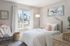 Bright and cozy bedroom with charming decor, featuring a fluffy chair, wicker basket, and pastel wall art, overlooking a lush garden view.