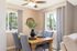 Charming dining area with elegant wooden table, plush grey chairs, and natural light streaming through large windows.