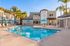 Luxurious apartment community with a pristine swimming pool, surrounded by palm trees and modern architecture under clear blue skies.