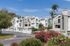 Charming apartment community with modern architecture, lush landscaping, and vibrant floral accents under a clear blue sky.