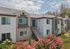 Charming apartment community with modern architecture, lush landscaping, and vibrant pink flowers under a sunny sky.