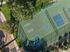 Aerial view of a modern sports complex with dual tennis courts surrounded by lush greenery and well-maintained pathways.