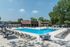 Luxurious outdoor pool area with sun loungers and shaded dining tables, surrounded by lush greenery and modern facilities.