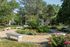 Charming garden view featuring lush greenery, vibrant flowers, and inviting benches surrounded by mature trees, perfect for relaxation and outdoor enjoyment.