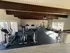 Bright and inviting apartment gym with modern fitness equipment, large windows, and wooden beams creating a welcoming workout space.