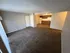 Inviting open-plan apartment featuring a spacious carpeted living area leading to a cozy kitchen with wood cabinetry.
