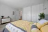 Inviting bedroom with modern decor, featuring a cozy bed with yellow and gray bedding, sleek white closets, and stylish mid-century dresser.