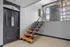 Inviting apartment entryway with a stylish black door labeled '1A', featuring brick walls and modern wooden stairs leading to bright natural light.