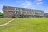 Charming brick apartment building with private balconies set against a vibrant green lawn and blue sky.