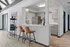 Bright modern kitchen with sleek grey cabinets, stainless steel refrigerator, and cozy breakfast bar with stylish chairs, complemented by a popcorn machine for entertaining.