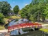 Idyllic apartment complex with a charming red footbridge spanning a tranquil pond, surrounded by lush greenery and a serene atmosphere.