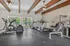 Bright and inviting home gym with modern exercise equipment, large windows offering lush garden views, and rustic wooden ceiling beams.