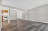 Modern open-concept living area with elegant wood-style flooring and natural light, connected to a cozy kitchen with classic cabinetry and white appliances.