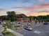 Charming apartment complex at sunset with warm illuminated windows and lush greenery, featuring ample parking and serene surroundings.