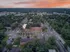 Aerial view of a charming apartment complex surrounded by lush greenery, featuring picturesque streets and vibrant sunset skies.