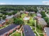 Aerial view of a beautiful apartment community featuring lush green lawns, mature trees, and a central swimming pool, surrounded by charming brick buildings.