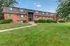 Charming brick apartment building surrounded by lush greenery and a well-maintained lawn, offering a cozy and inviting community setting.