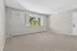 Bright and spacious living room featuring plush carpeting, large window with a serene garden view, and sleek air conditioning unit for comfort.
