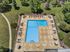 Luxurious outdoor pool area with elegant lounge chairs and umbrellas, surrounded by lush green landscape and a walking path.