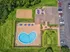 Aerial view of a luxurious apartment complex featuring a heart-shaped swimming pool, spacious patio with umbrellas, and lush green surroundings next to a sand volleyball court.