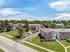 Charming aerial view of a suburban apartment complex with lush green lawns, ample parking, and tranquil surroundings under a bright blue sky.