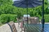 Charming outdoor patio with elegant furniture, large umbrella, and lush greenery, ideal for relaxing and entertaining.