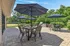 Charming outdoor patio with multiple dining sets under large umbrellas, surrounded by lush greenery and a barbecue area, perfect for entertaining and relaxation.