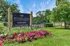 Vibrant Woodlands of Crest Hill Apartments leasing center sign surrounded by lush greenery and colorful flower beds.