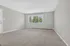 Bright and spacious living room with plush carpeting, large window showcasing greenery, and sleek air conditioning unit.