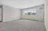 Bright and spacious living room with large window, plush carpet, and modern air conditioning unit.