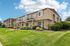 Charming apartment complex with rustic stone facade, lush green landscaping, and inviting balconies under a blue sky.