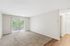 Bright and spacious living room with large window and sliding doors to a garden view balcony, featuring cozy carpet flooring and neutral walls.