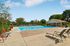 Inviting outdoor pool area with comfortable lounge chairs, vibrant greenery, and a charming pool house under a clear blue sky.