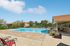 Inviting outdoor swimming pool area with sun loungers, surrounded by lush greenery and charming residential buildings under a bright blue sky.