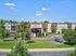 Charming apartment complex with lush greenery, stylish balconies, and ample parking, set against a stunning clear blue sky.