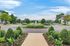Immaculately landscaped garden path leading to a vibrant central fountain with scenic views and ample parking.