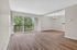 Bright and airy living room with stylish wood flooring, large windows, and a view of lush greenery.