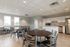 Modern communal dining area with sleek round tables, stainless steel appliances, and ample natural light from large windows.
