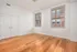 Bright and inviting room with elegant hardwood flooring, featuring large windows that offer ample natural light and a charming view of the brick building outside.