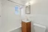 Inviting bathroom featuring white tiles, a bathtub, a modern sink with wooden vanity, and natural light from a window.
