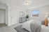 Bright and airy bedroom with neutral decor, featuring a cozy bed, elegant dresser, and large window view.