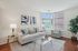 Bright and inviting living room with a modern gray sofa, elegant glass coffee table, and large windows flooding the space with natural light.