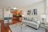 Modern, open-concept living room with elegant kitchen, featuring stylish wooden cabinets, stainless steel appliances, and cozy seating area enhanced by tasteful artwork.